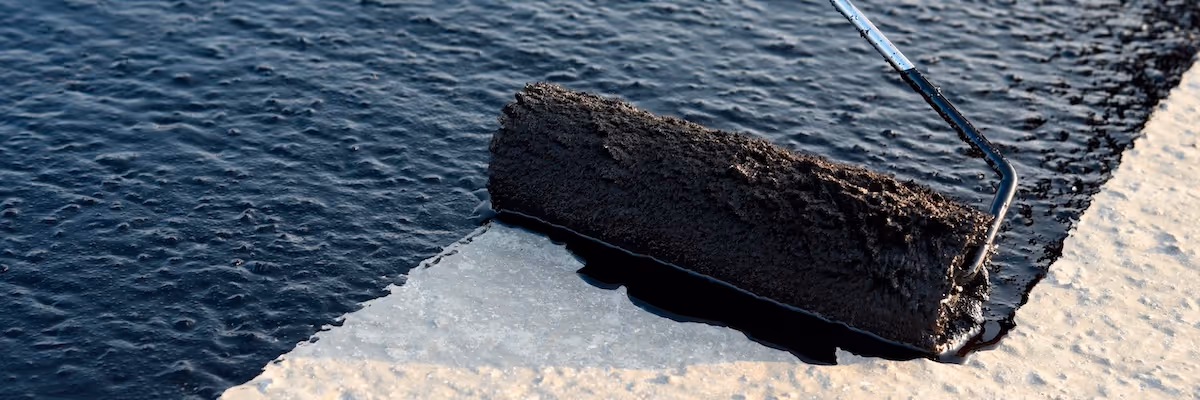 Close-up of a roller applying roof coating to a flat surface