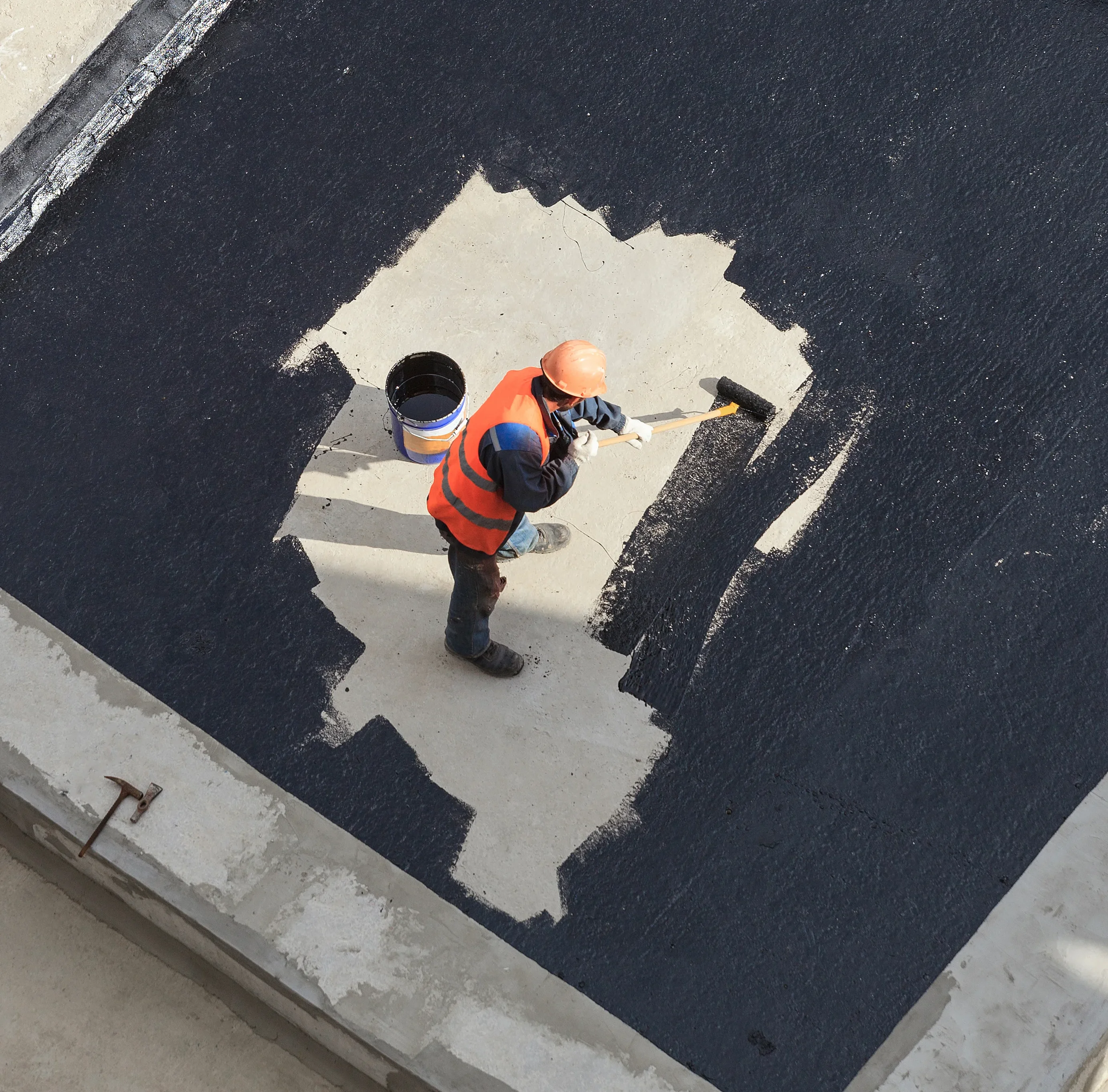 Roofer applying silicone coating to repair a damaged section of a flat commercial roof
