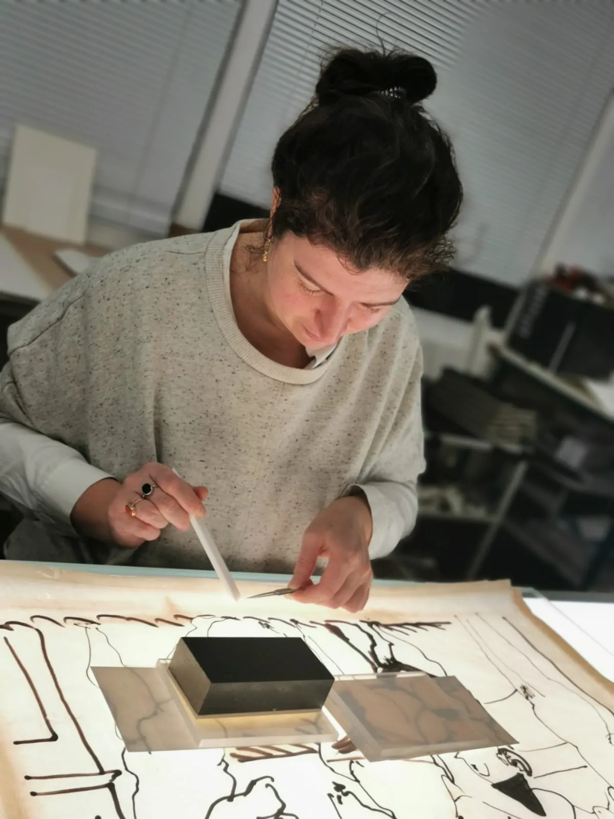 Femme avec un chignon travaillant attentivement sur un dessin ou croquis à la table lumineuse avec des outils de dessin.