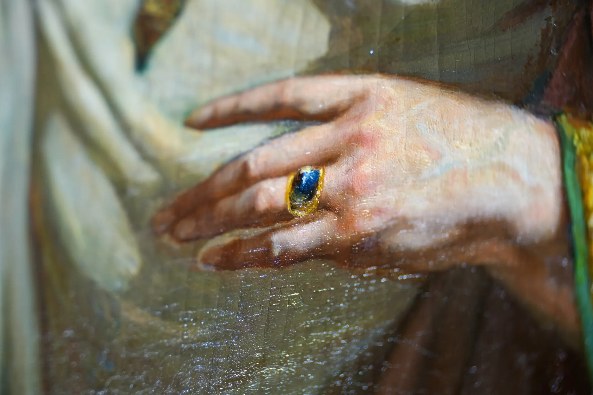 Détail d'une peinture montrant une main avec une bague dorée sertie d'une pierre bleue.