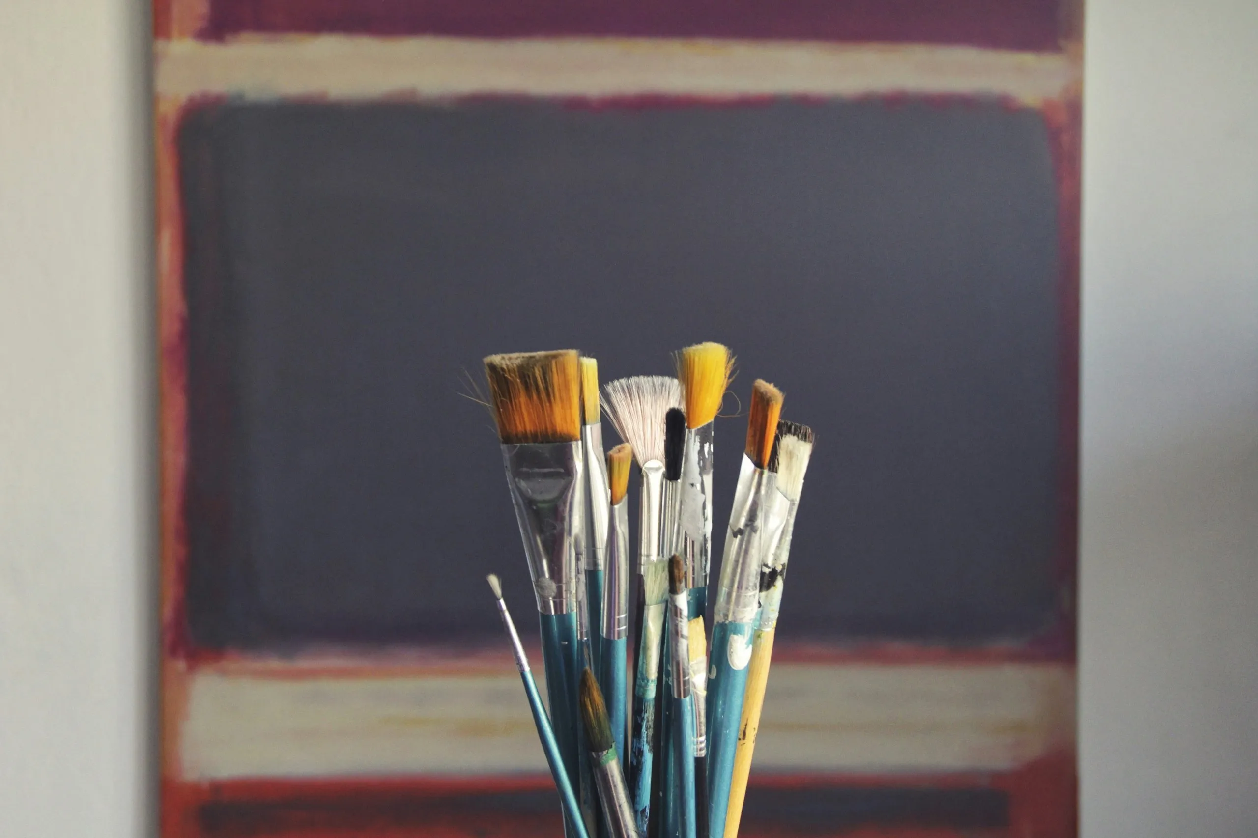 Groupe de pinceaux de peinture usés devant une toile de style abstrait avec des rectangles colorés.