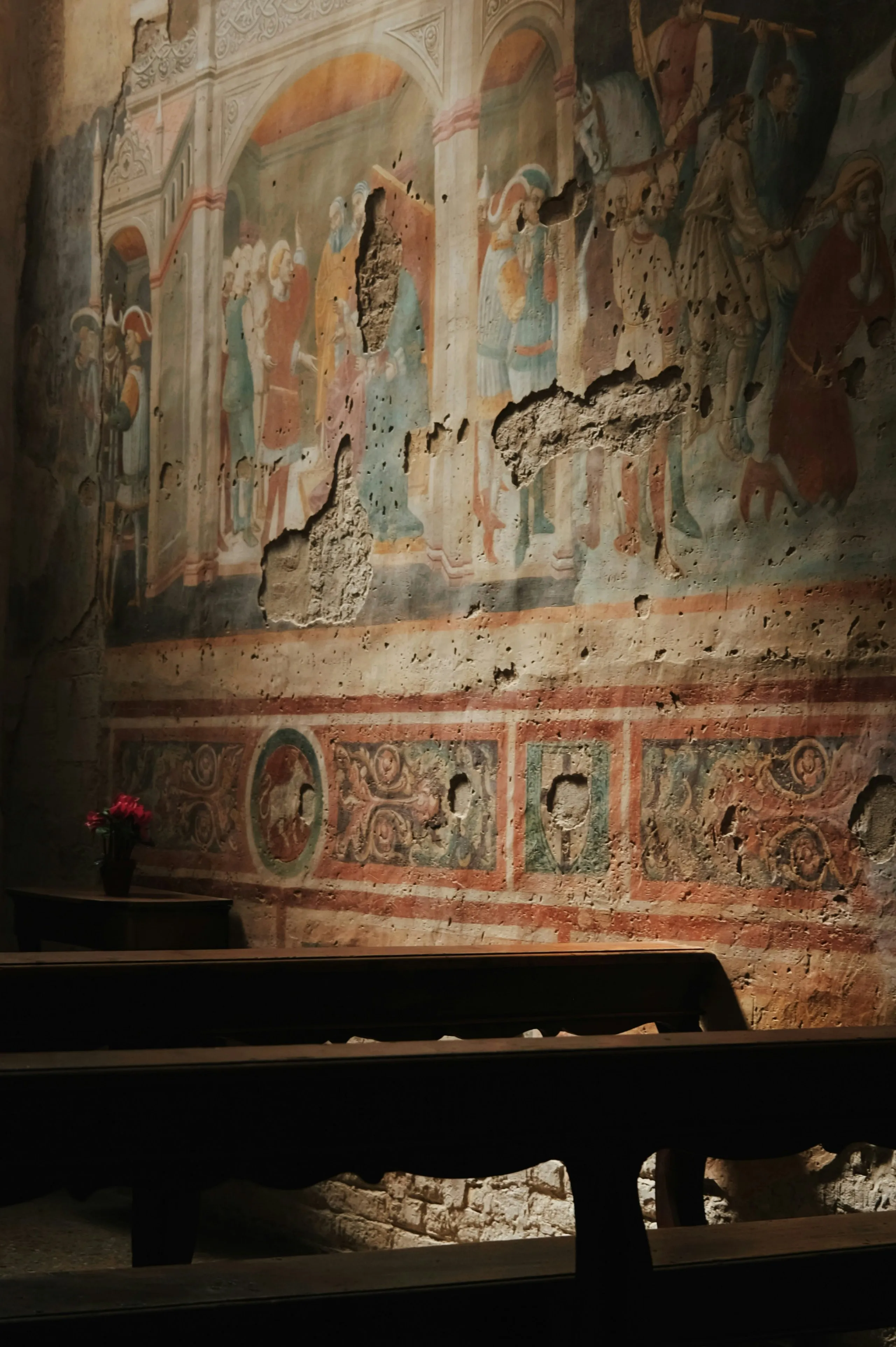 Mur peint ancien endommagé avec fresque médiévale dans une église, bancs en bois à l'avant-plan.