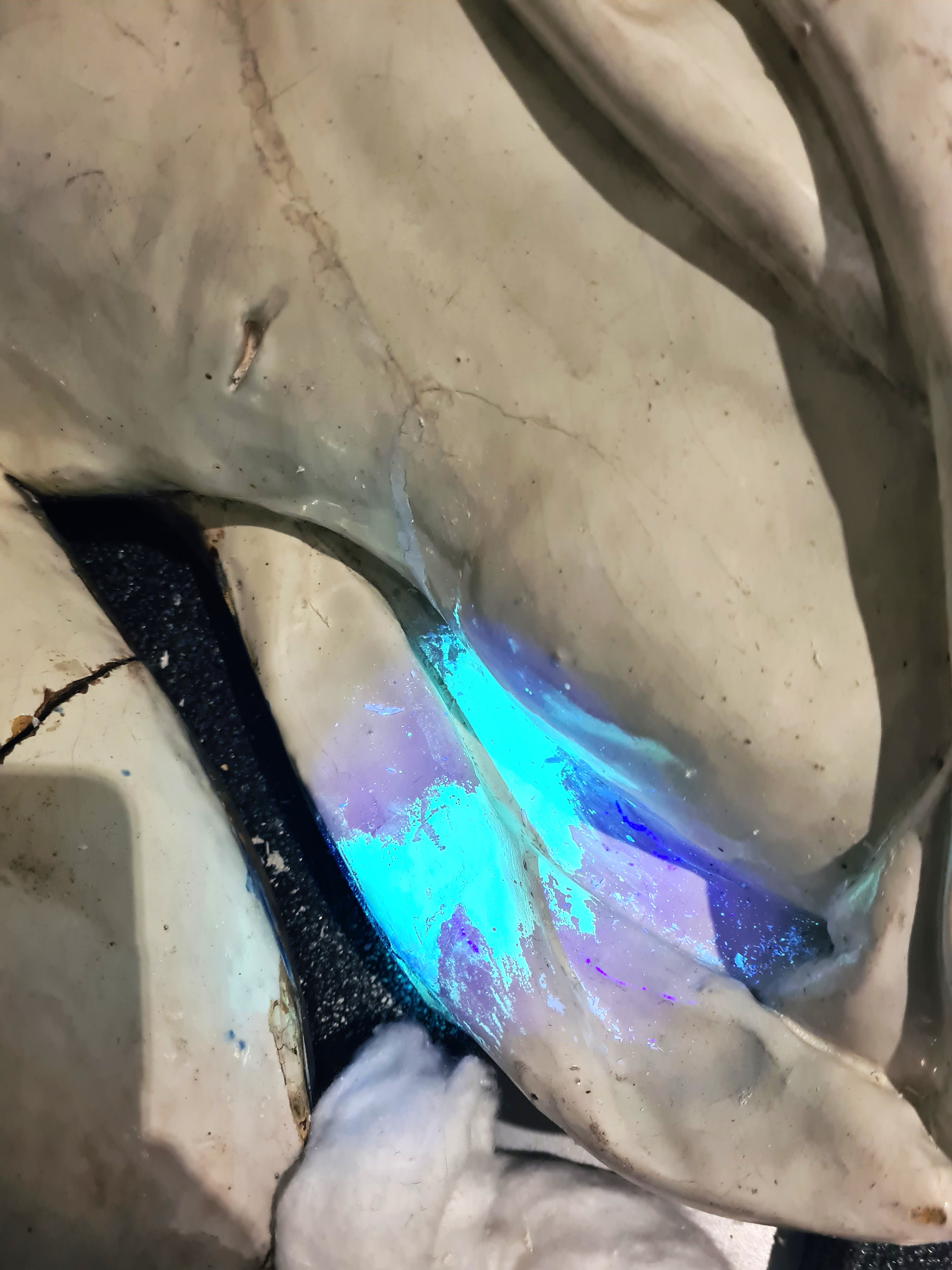 Surface d'une sculpture avec une zone éclairée en bleu fluorescent sous lumière UV.