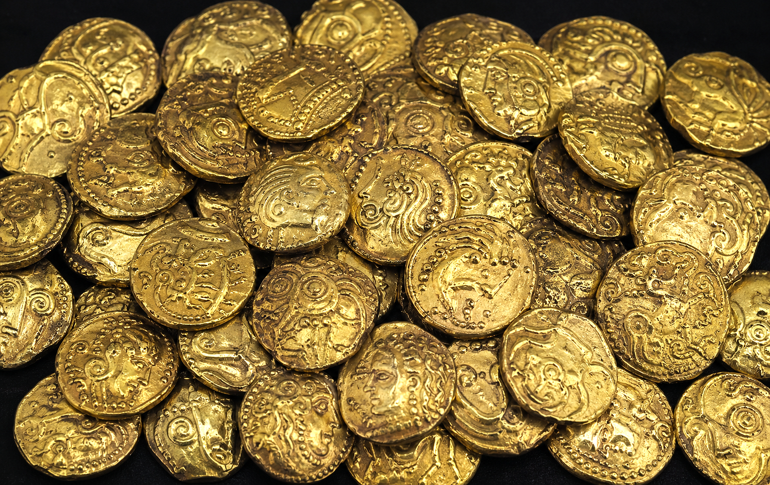 Pile de pièces antiques en or avec des gravures de visages et motifs sur fond noir.