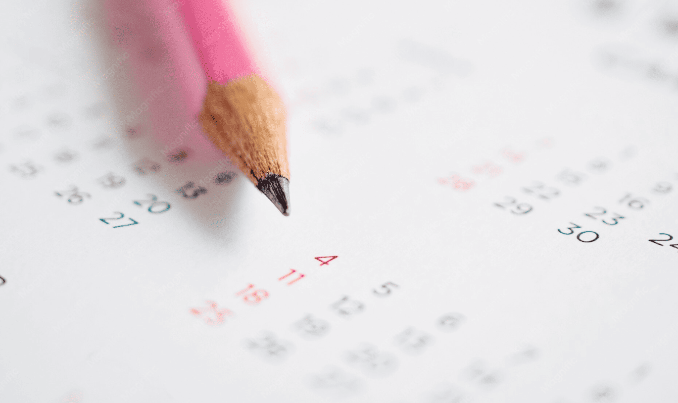 Gros plan d'un crayon rose pointu posant sur un calendrier imprimé.
