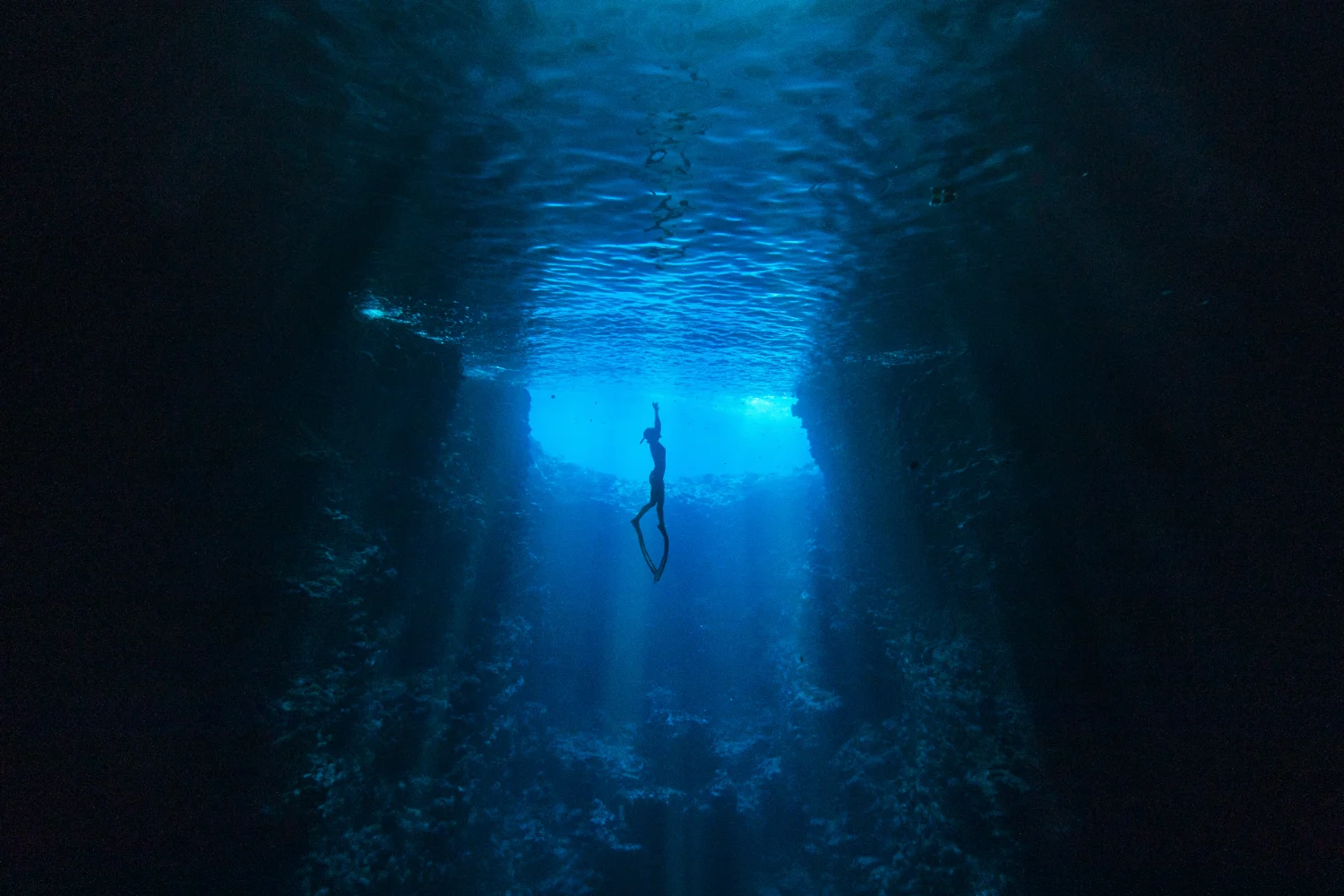 Person in einem Taucheranzug schwebt in tiefblauem Wasser mit Licht von oben