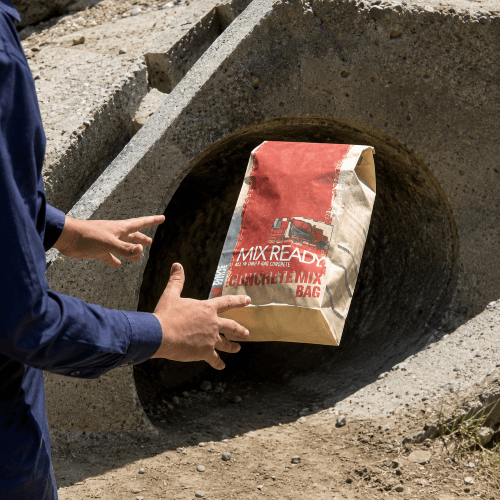 Worker holding a Mix Ready all-purpose concrete mix bag at a culvert
