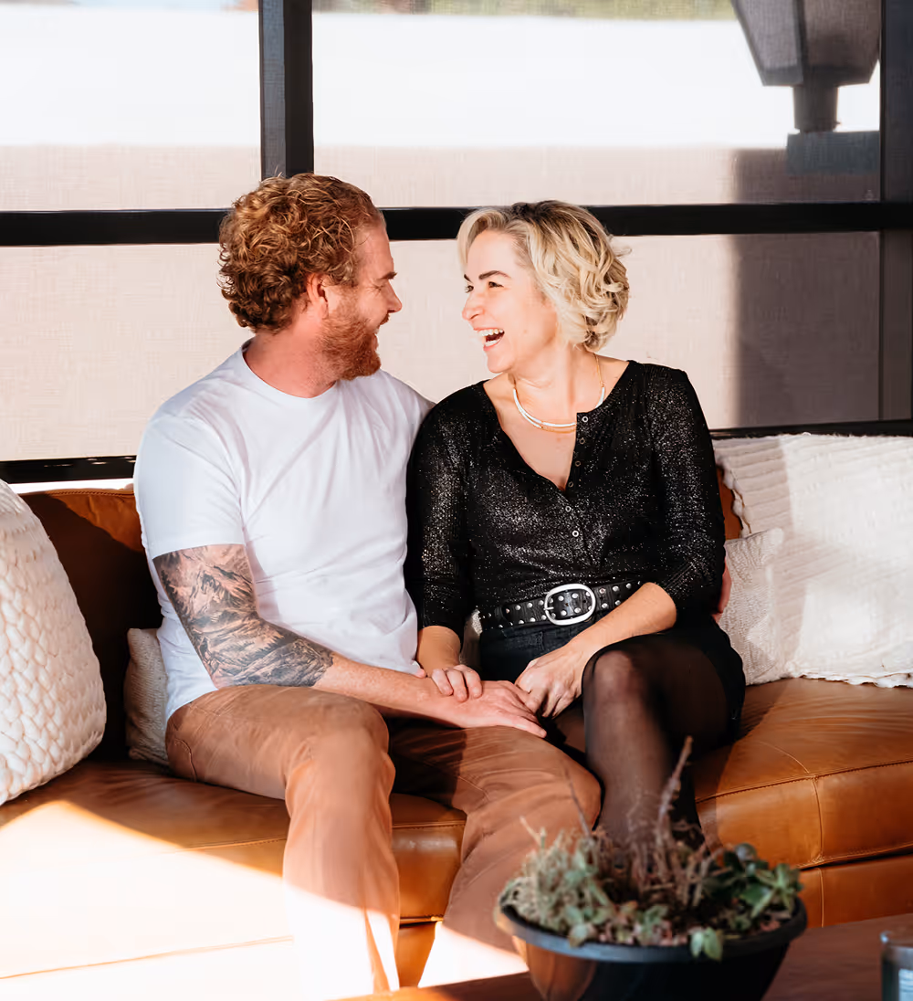 doug and lindsey smiling sitting on brown couch 1