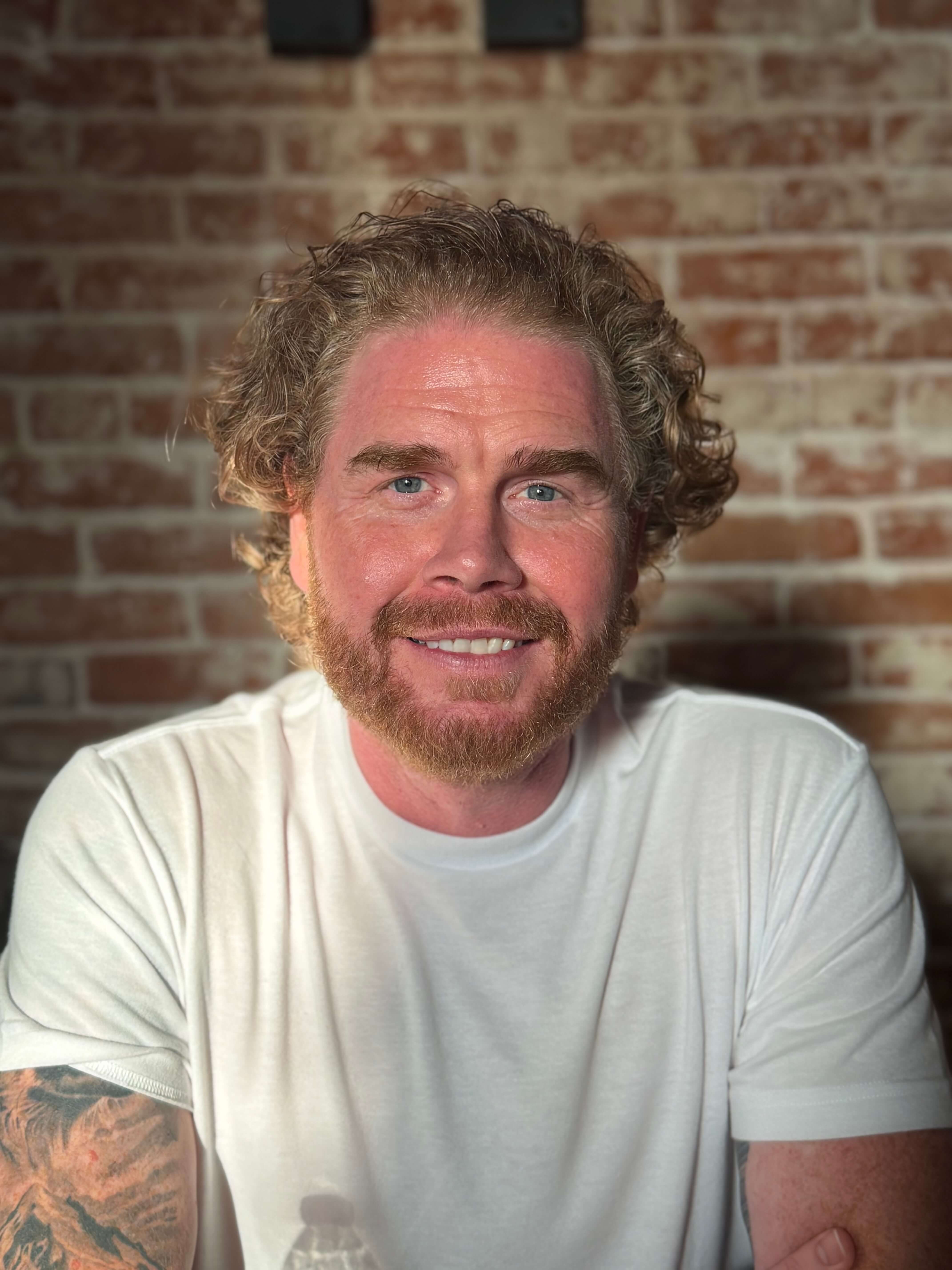 Doug smiling at camera in front of brick wall