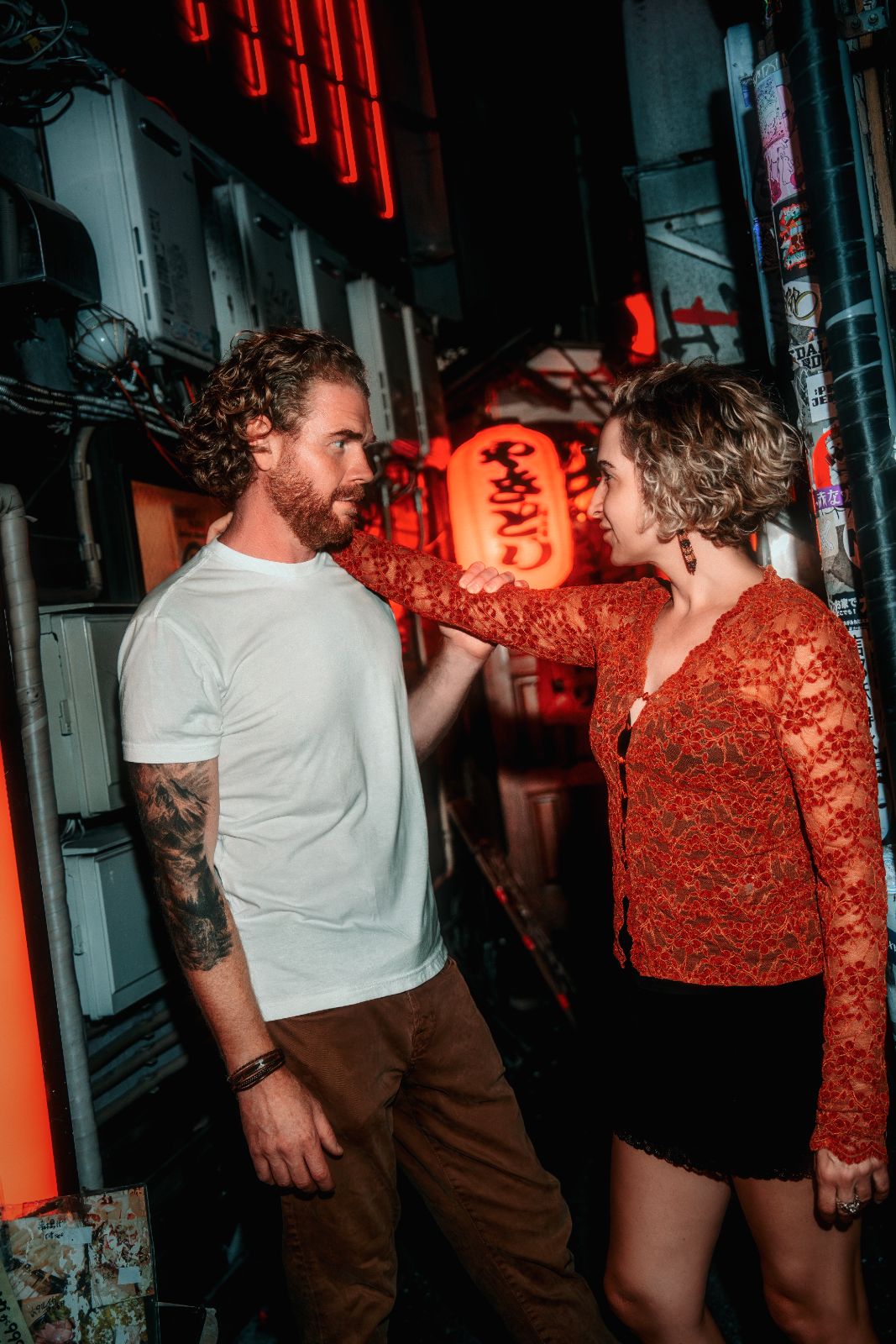 A woman reaching for her husband in a neon-lit alley at night