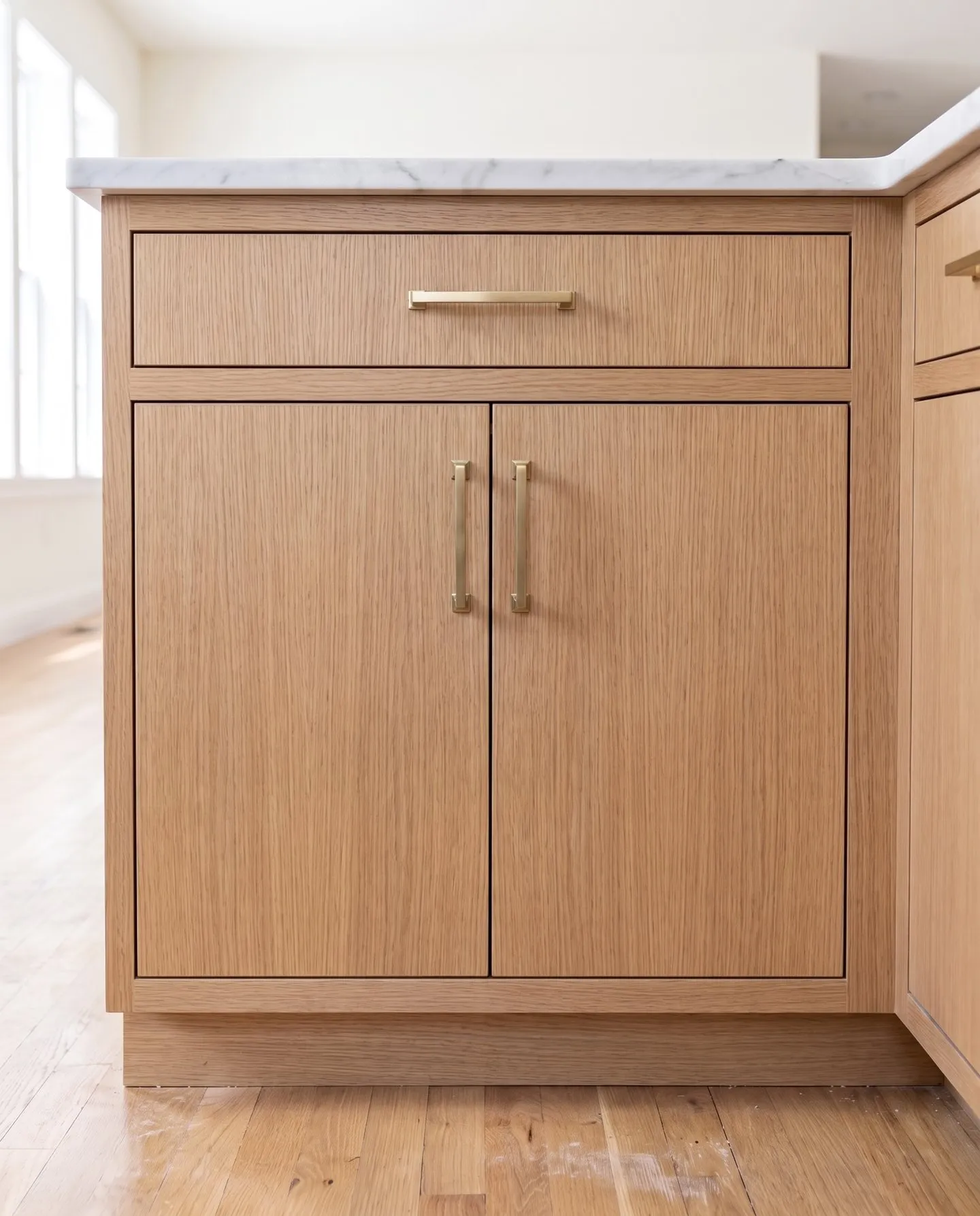 Flat-panel base cabinet in natural white oak, plain slab doors with straight grain and brass pulls