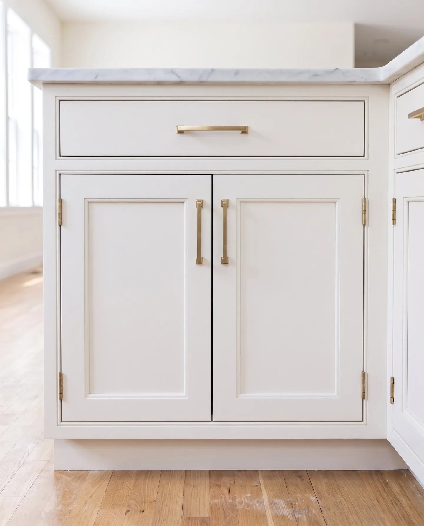 Warm white inset base cabinet, doors set flush inside a beaded face frame on exposed brass hinges, with brass pulls