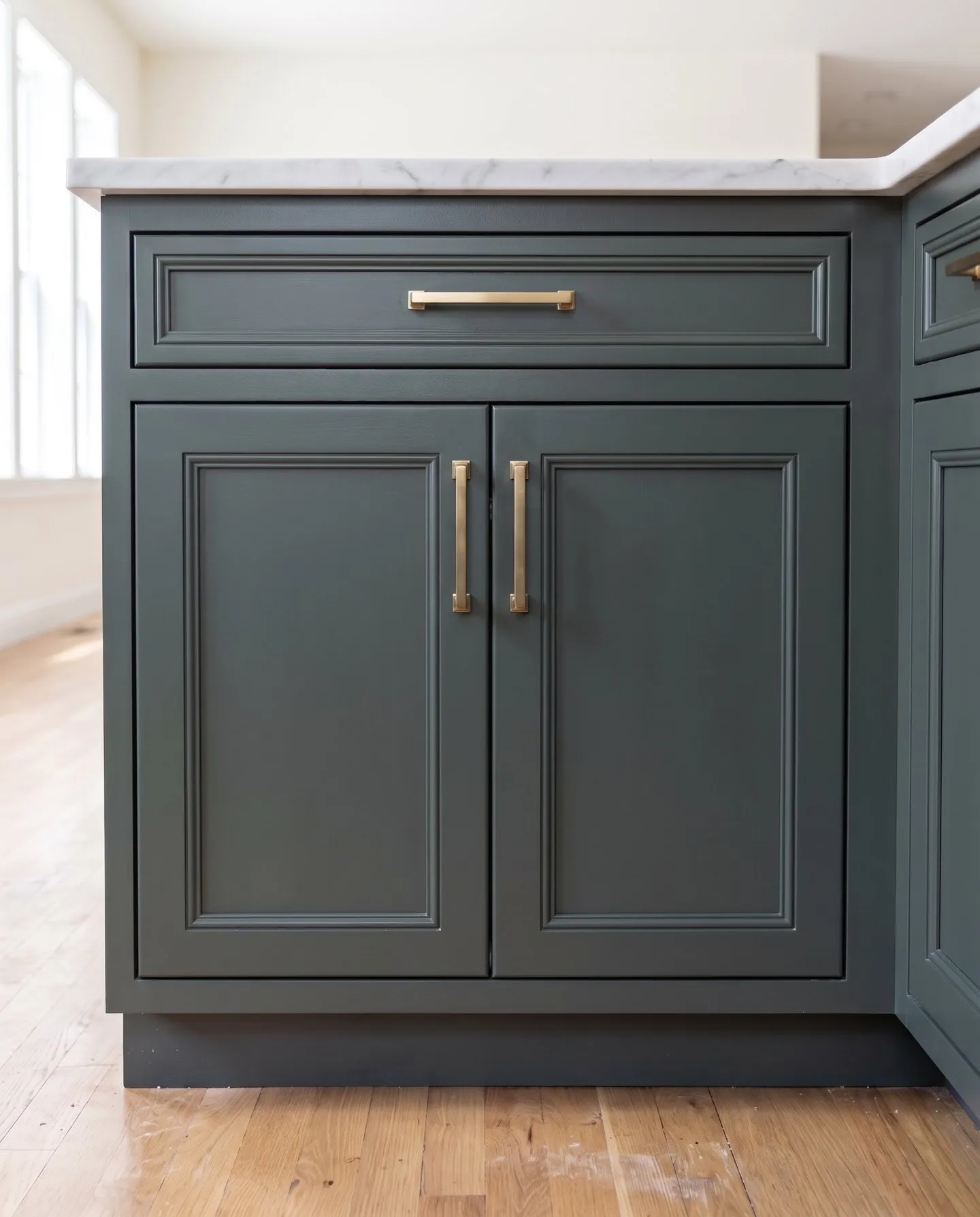Green-gray base cabinet with moulding applied around each recessed door panel, with brass pulls