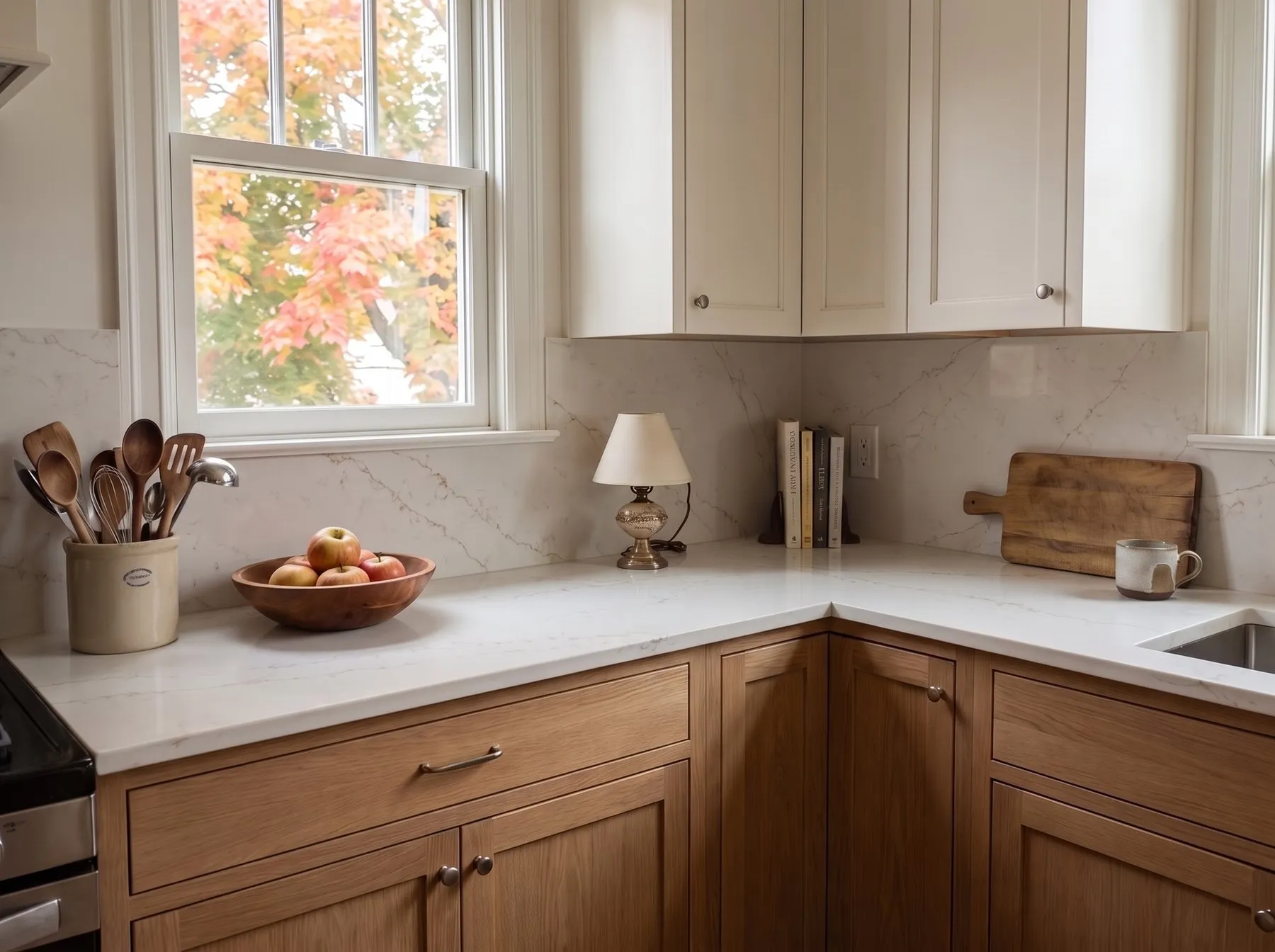 Warm white veined countertop and matching backsplash on natural oak cabinets, with a bowl of apples and a crock of wooden spoons