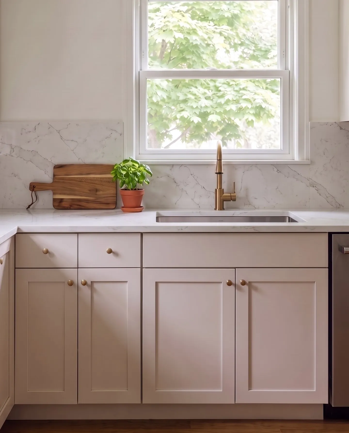 White countertop and backsplash with soft gray veining above warm white shaker cabinets with brass knobs