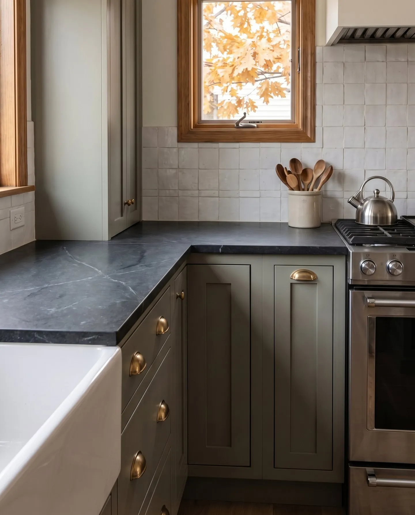 Dark charcoal matte countertop on green-gray shaker cabinets with brass cup pulls and a white tile backsplash