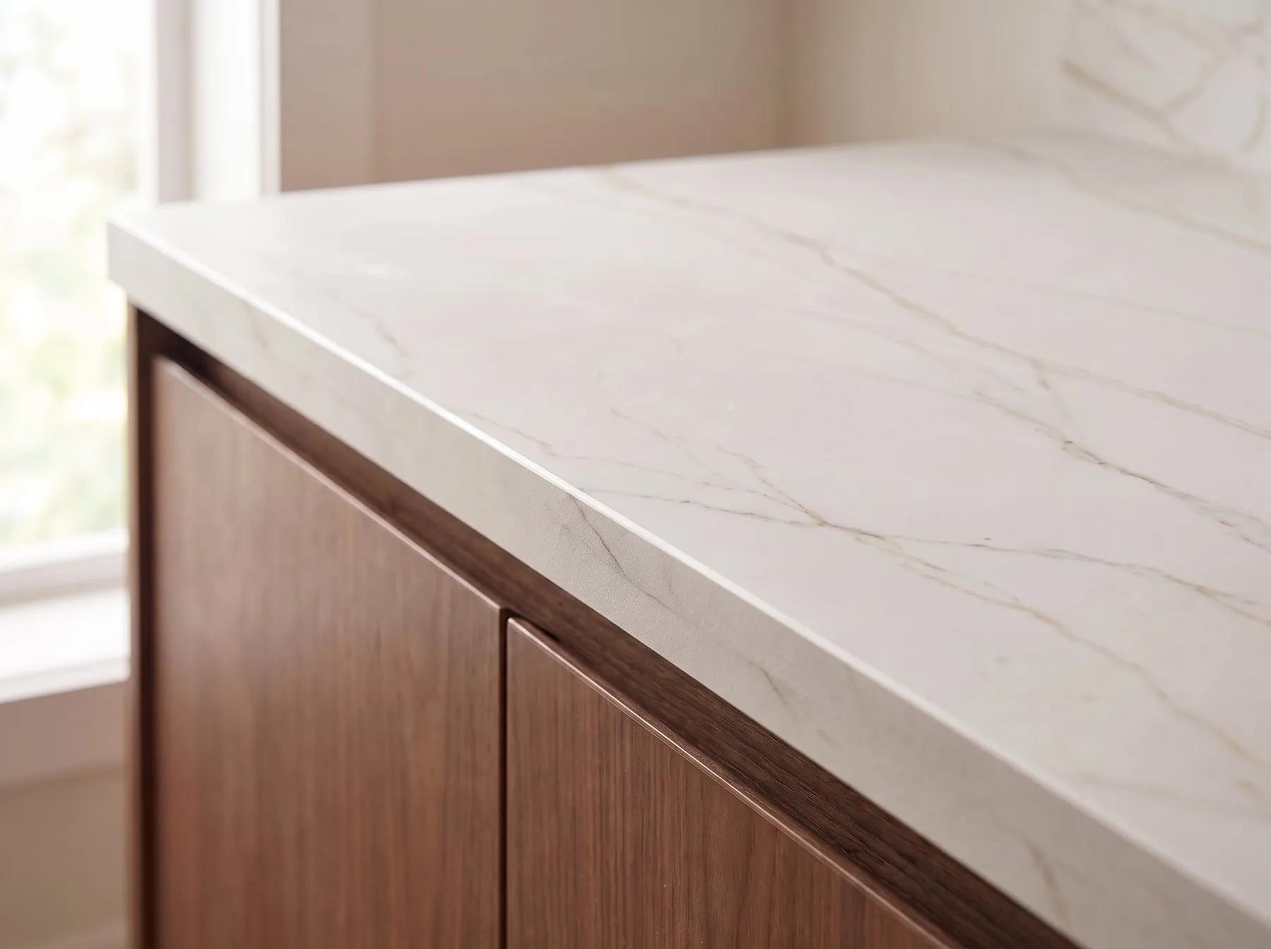 Thin matte porcelain countertop in warm white with fine veining on flat-panel walnut cabinets