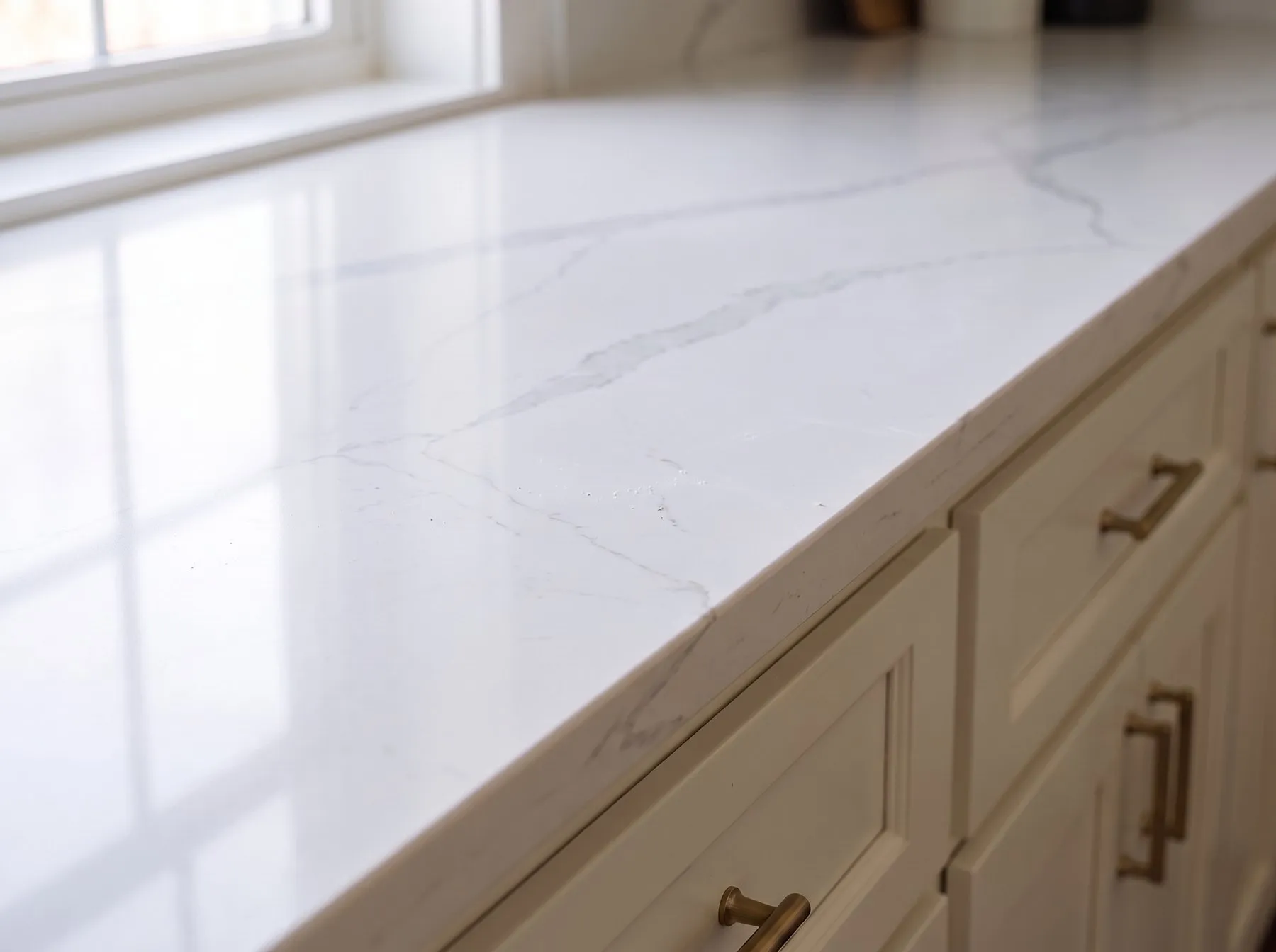 Polished white quartz countertop with consistent gray veining, seen across the counter toward a window