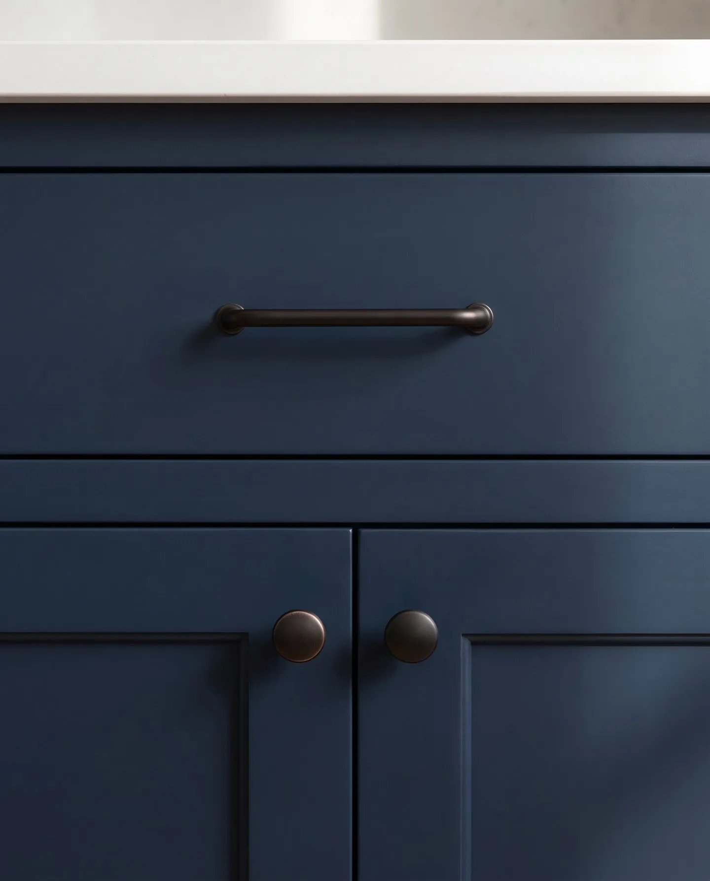 Blackened bronze bar pull and knobs on navy painted cabinet fronts