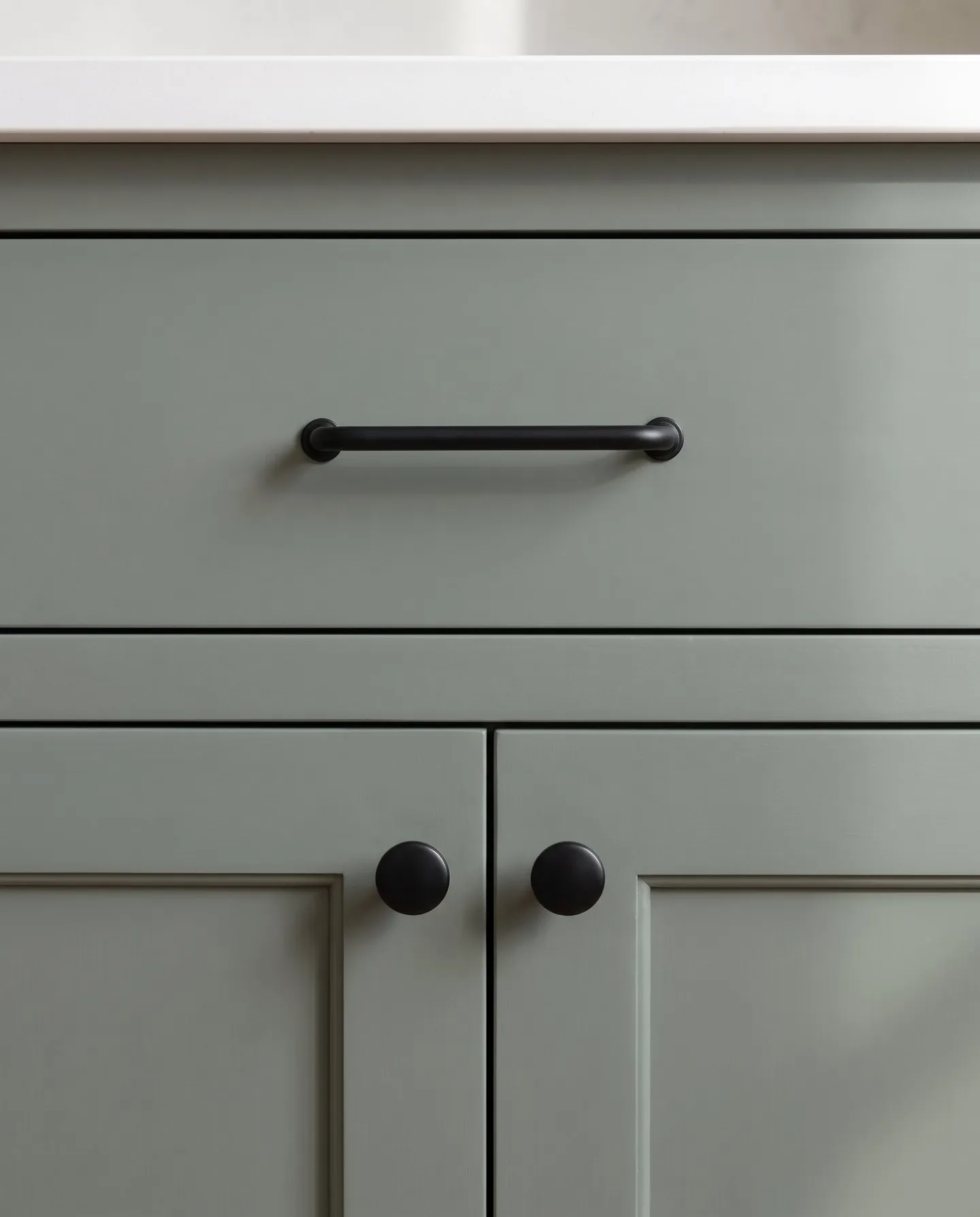 Matte black bar pull and knobs on green-gray painted cabinet fronts