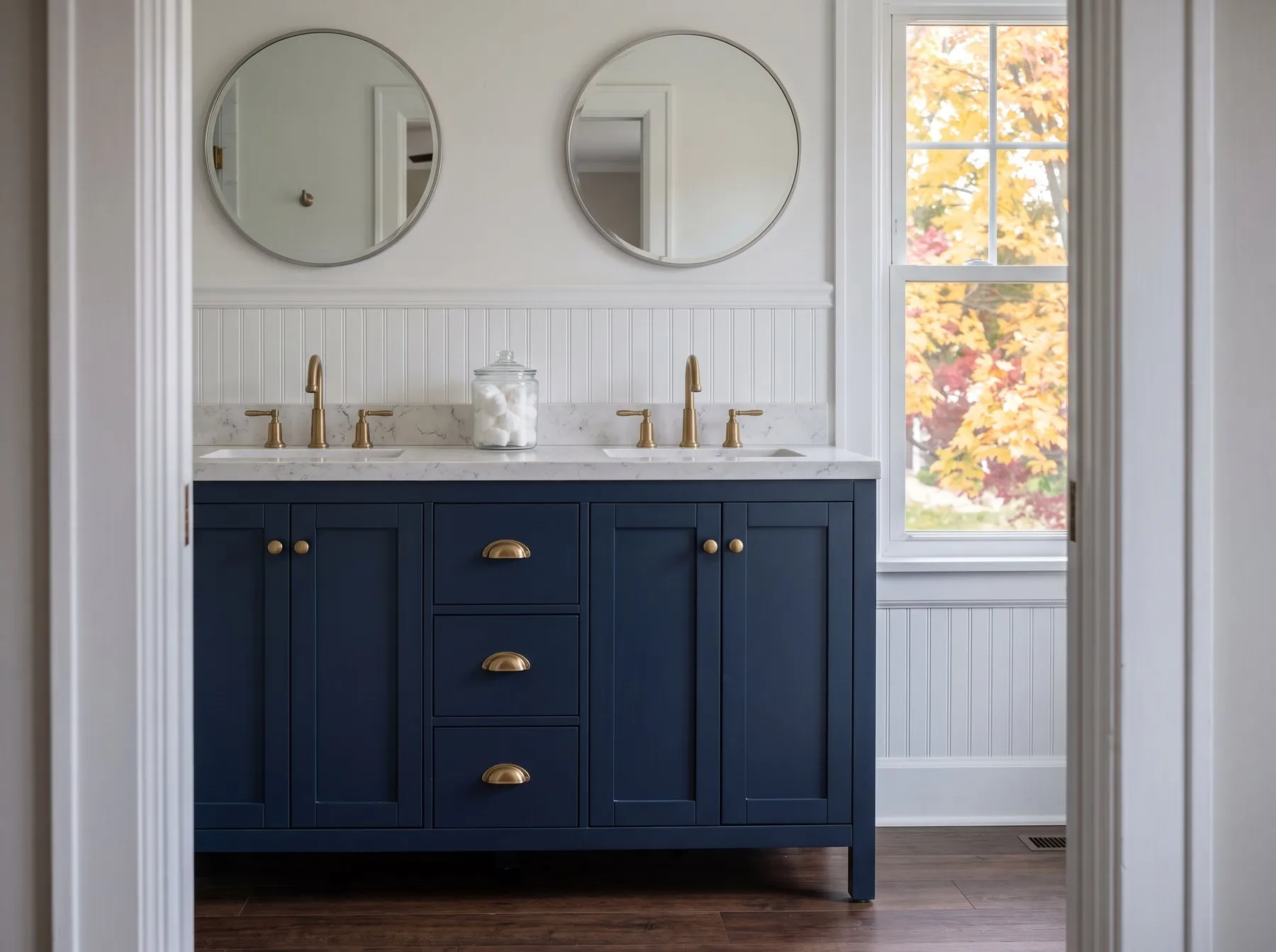 Navy double-basin shaker vanity with brass cup pulls and knobs under two round mirrors