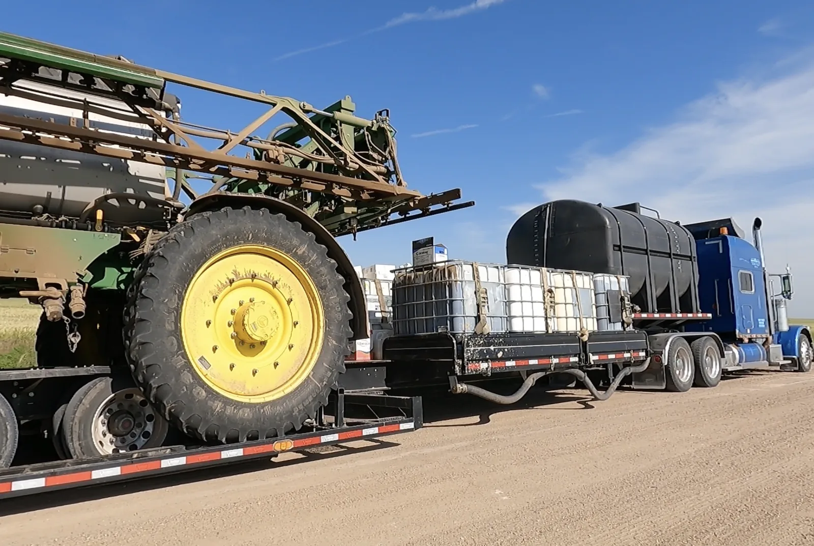 Field fill: tender trailer alongside a sprayer, totes strapped on deck