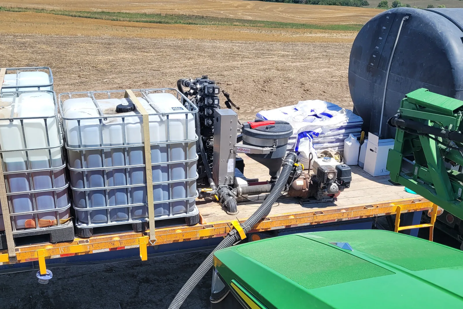 Flatbed with totes, dry product, and Fusion Inductor loading a sprayer in the field