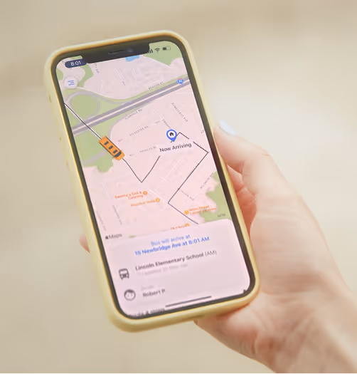 Hand holding a smartphone displaying a bus tracking app showing a bus on route and estimated arrival time at Lincoln Elementary School.