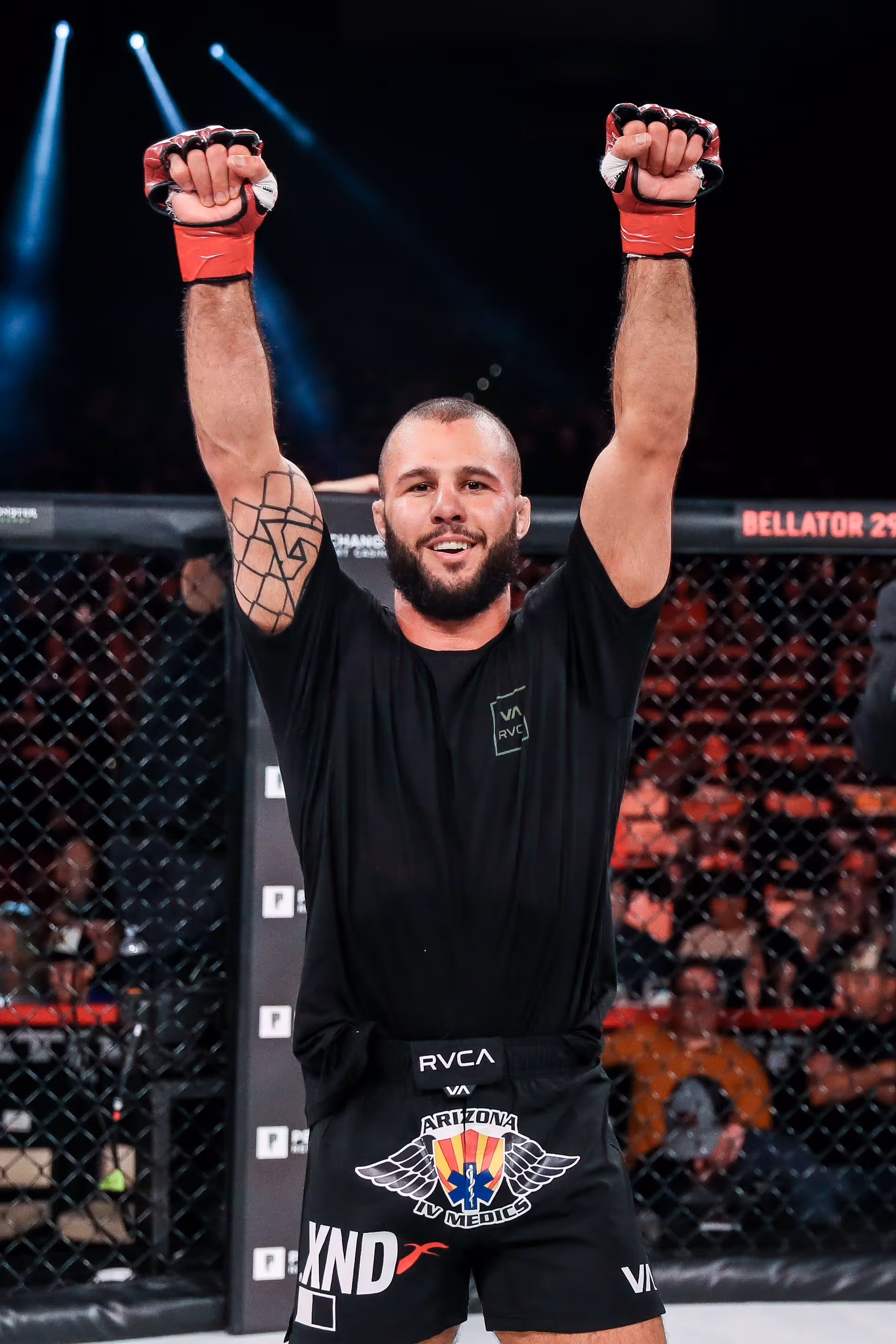 Mixed martial arts fighter with raised arms celebrating victory inside the cage.