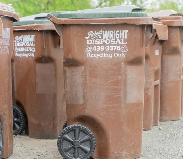 Brown recycling bins with wheels arranged outdoors labeled 'Robert Wright Disposal, Recycling Only' with phone number.