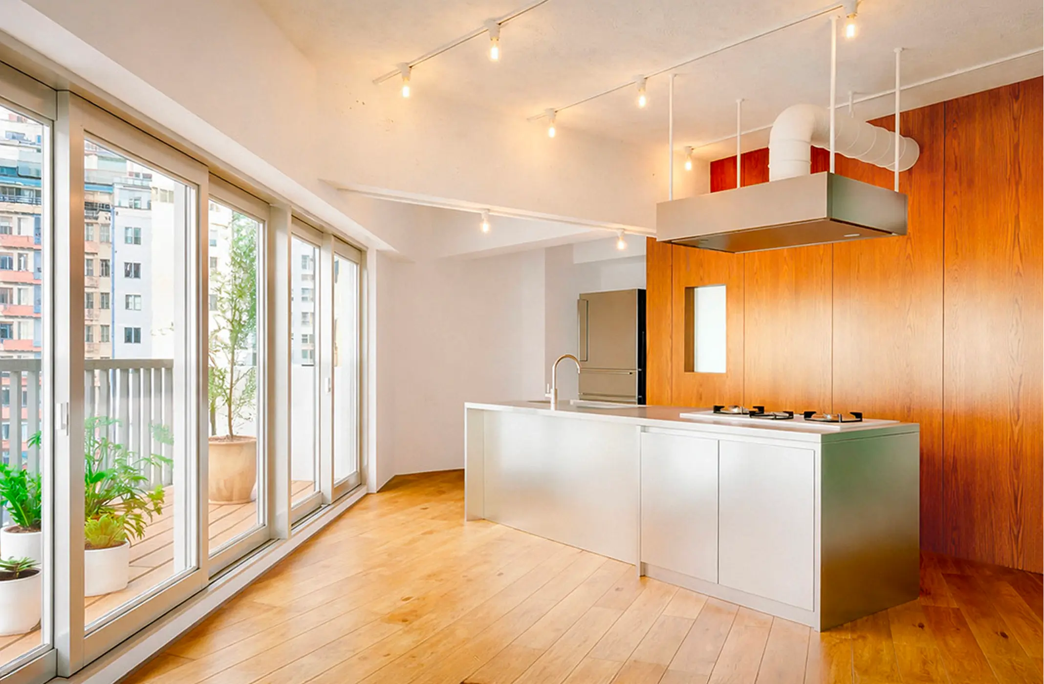 Modern kitchen with large windows, wooden floor, stainless steel island, and plants on balcony.