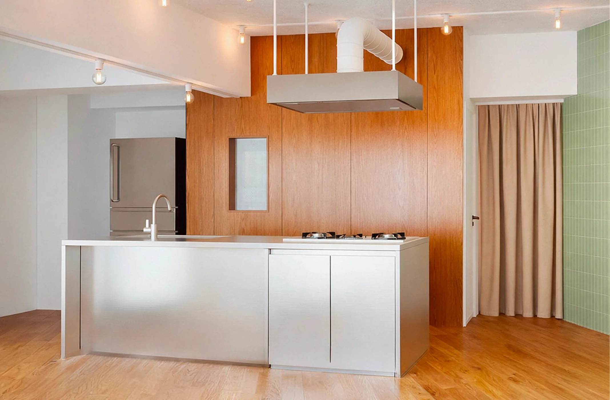 Modern kitchen with a stainless steel island, wooden wall, green tiled wall, and beige curtain.