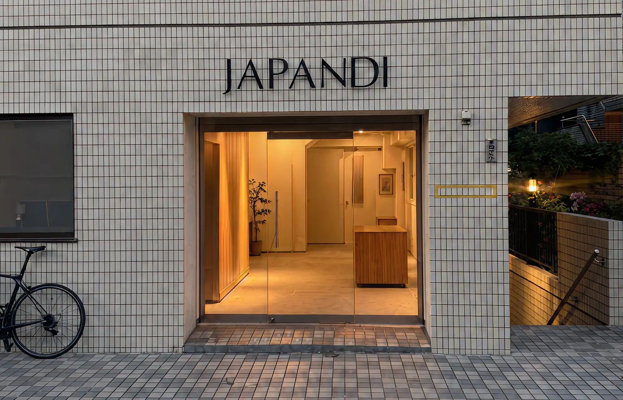 Entrance of a building named JAPANDI with glass doors, wooden reception, and tiled exterior walls.