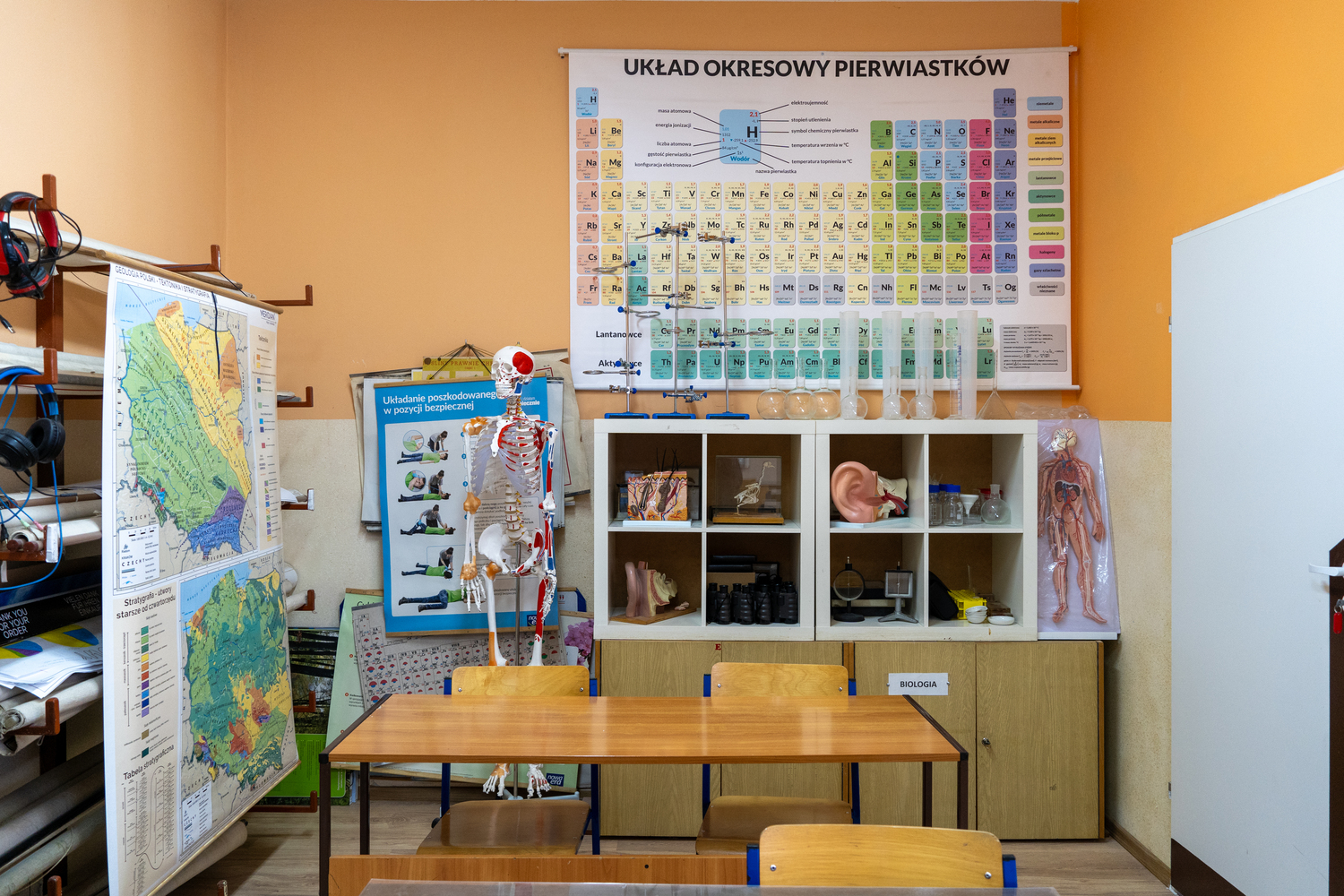 Teacher sitting on classroom floor showing colorful paper shapes to three young children engaged in group activity.