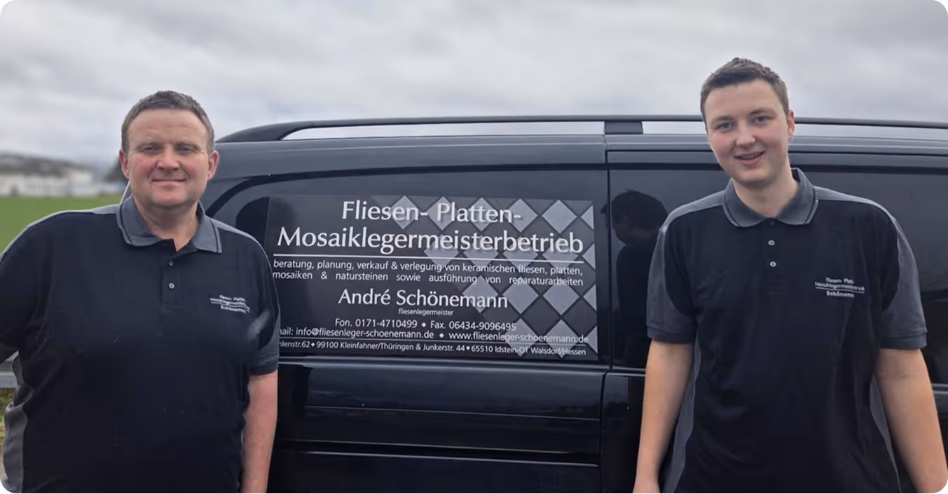 Zwei Männer in schwarzen Poloshirts stehen neben einem schwarzen Fahrzeug mit Beschriftung für einen Fliesen-, Platten- und Mosaiklegermeisterbetrieb.