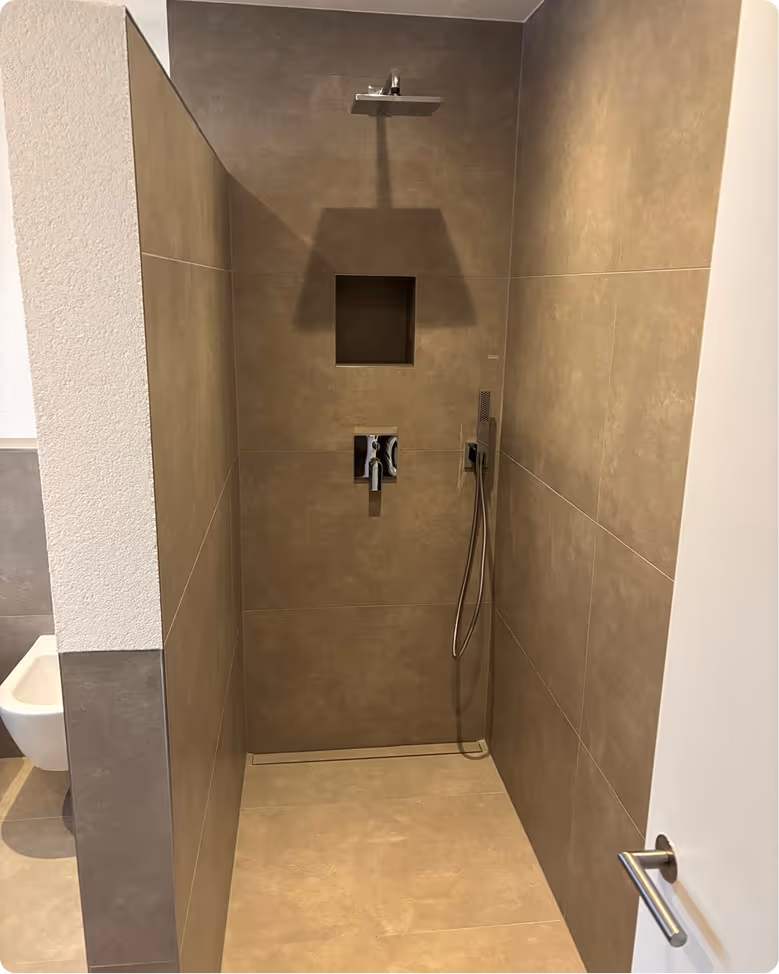 Moderne begehbare Dusche mit großem Regenduschkopf, Handbrause und eingebautem Ablagefach in braun-beigen Fliesen.