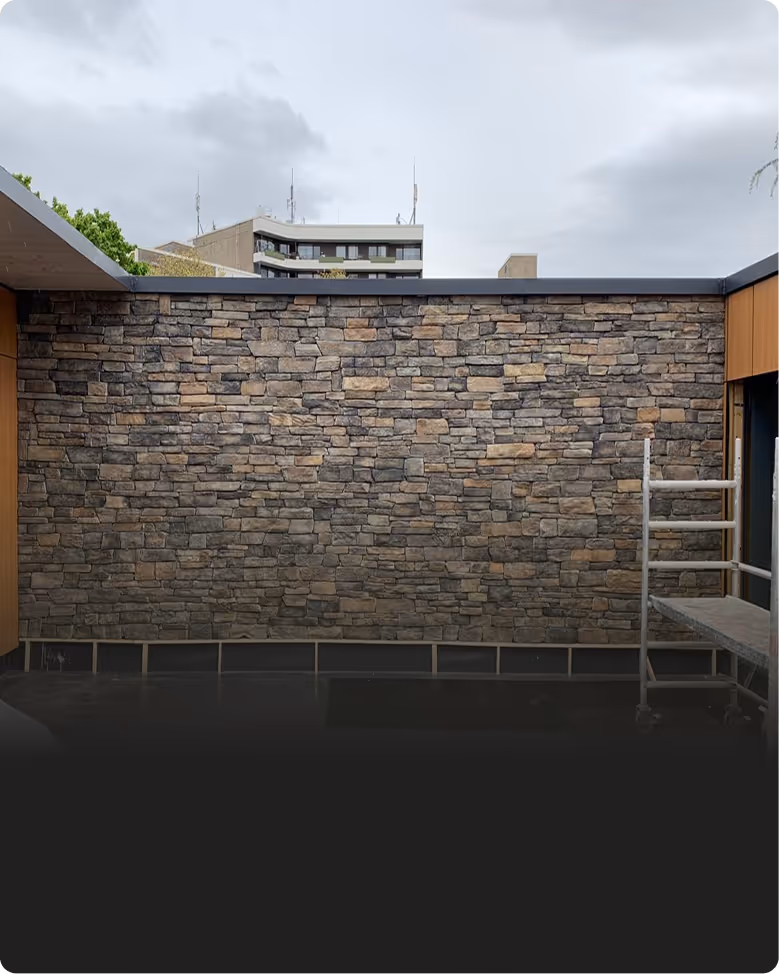 Fassade mit Natursteinmauer und einem Gerüst auf der rechten Seite unter bewölktem Himmel.