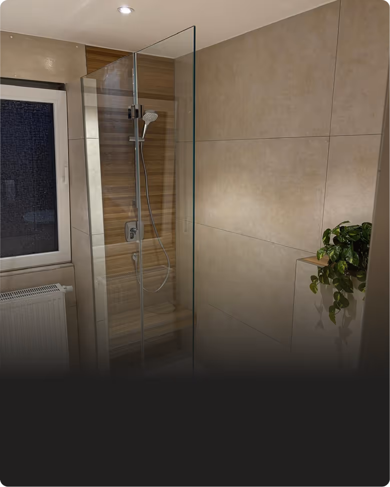Modernes Badezimmer mit ebenerdiger Dusche, Glasabtrennung und Holzvertäfelung, daneben ein kleiner grüner Topfpflanze.