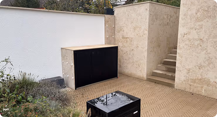 Moderner Außenbereich mit hellen Steinwänden, einer schwarzen Schrankeinheit und einer steinernen Treppe.
