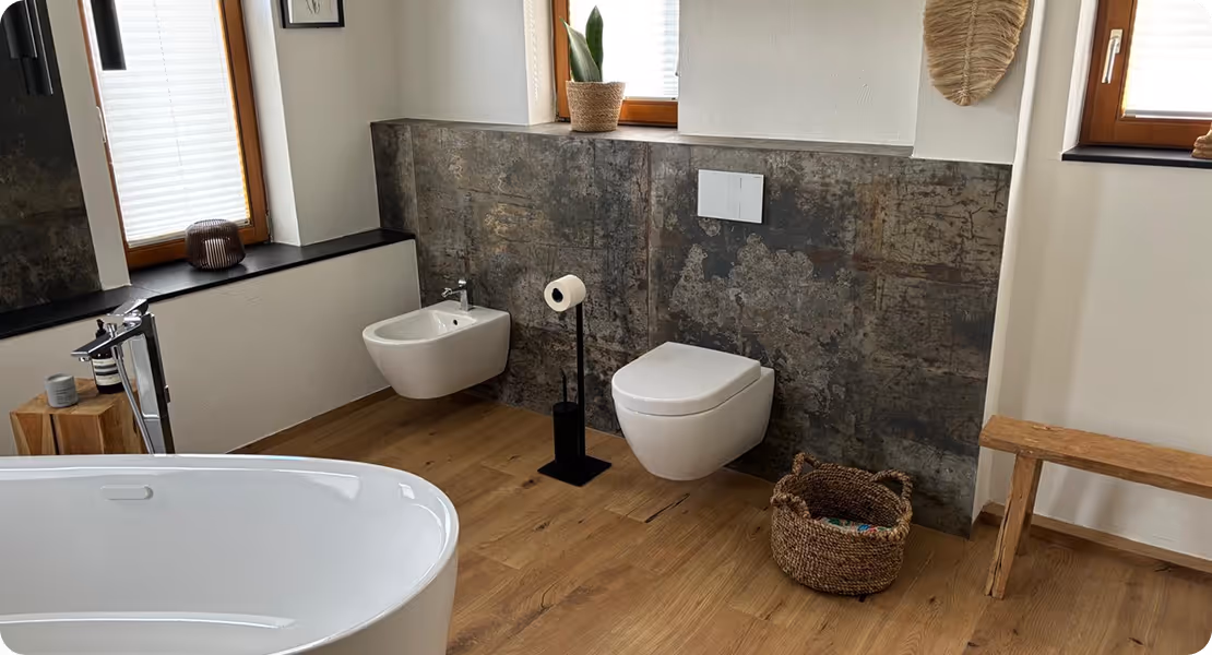 Modernes Badezimmer mit freistehender Badewanne, Wandtoilette, Bidet, Holzfußboden und großen Fenstern mit weißen Jalousien.