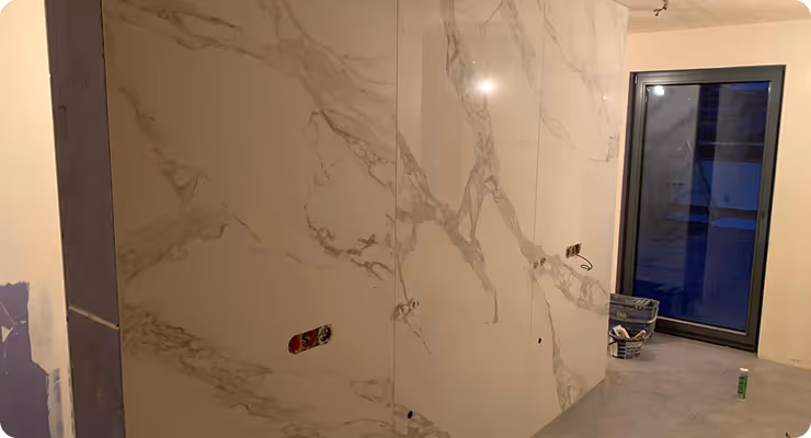 Raum mit großen weißen Wandplatten mit grauen Marmoradern, unvollendeter Bau mit offenem Stromanschluss und Glasfenster.