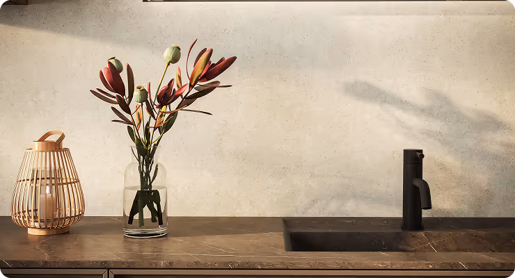 Moderner Küchentresen mit braunem Marmor, schwarzem Wasserhahn, Glasvase mit roten und grünen Blumen und einem Kerzenhalter aus Holz.