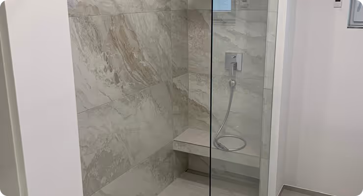 Moderne Dusche mit grauen Marmorfliesen und einer Glasabtrennung, ausgestattet mit einer Handbrause und einer Sitzbank.