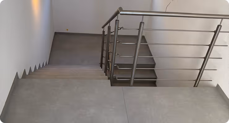 Blick auf eine moderne Treppe mit grauen Stufen und einem Edelstahlgeländer in einem weißen Innenraum.