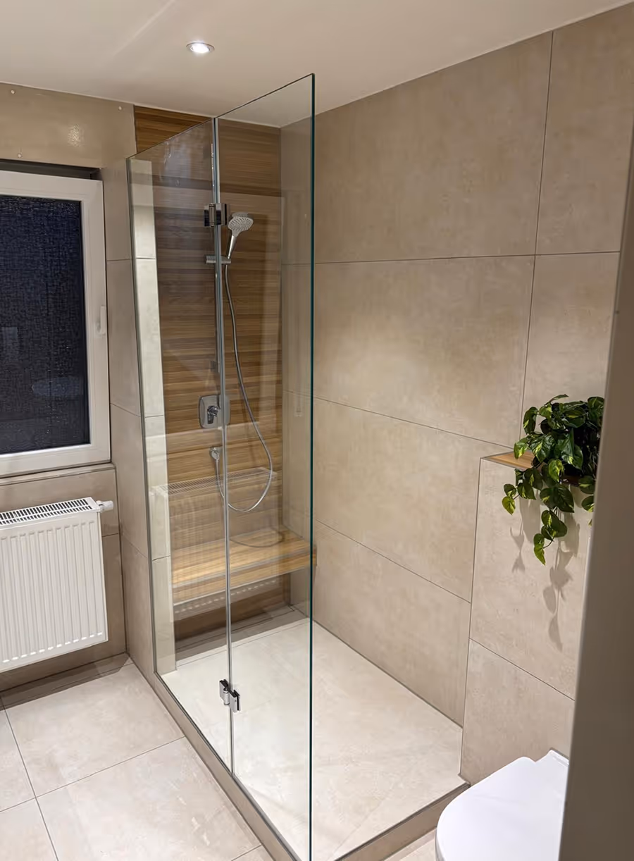 Modern bathroom with a glass shower enclosure, wood-paneled shower wall, white toilet, and a green potted plant on a tiled ledge.