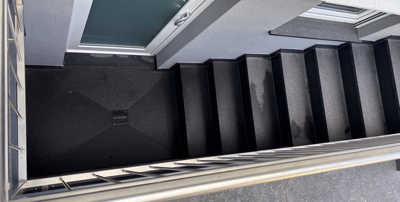 Abwärtstreppen mit schwarzem Boden und Metallgeländer neben einer Glastür.