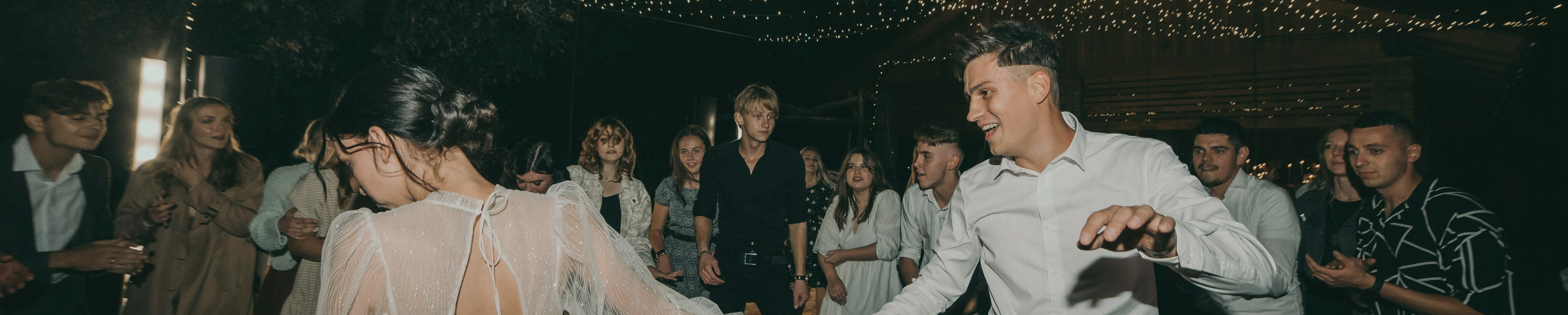 A group of people dancing and enjoying an outdoor night celebration under string lights.