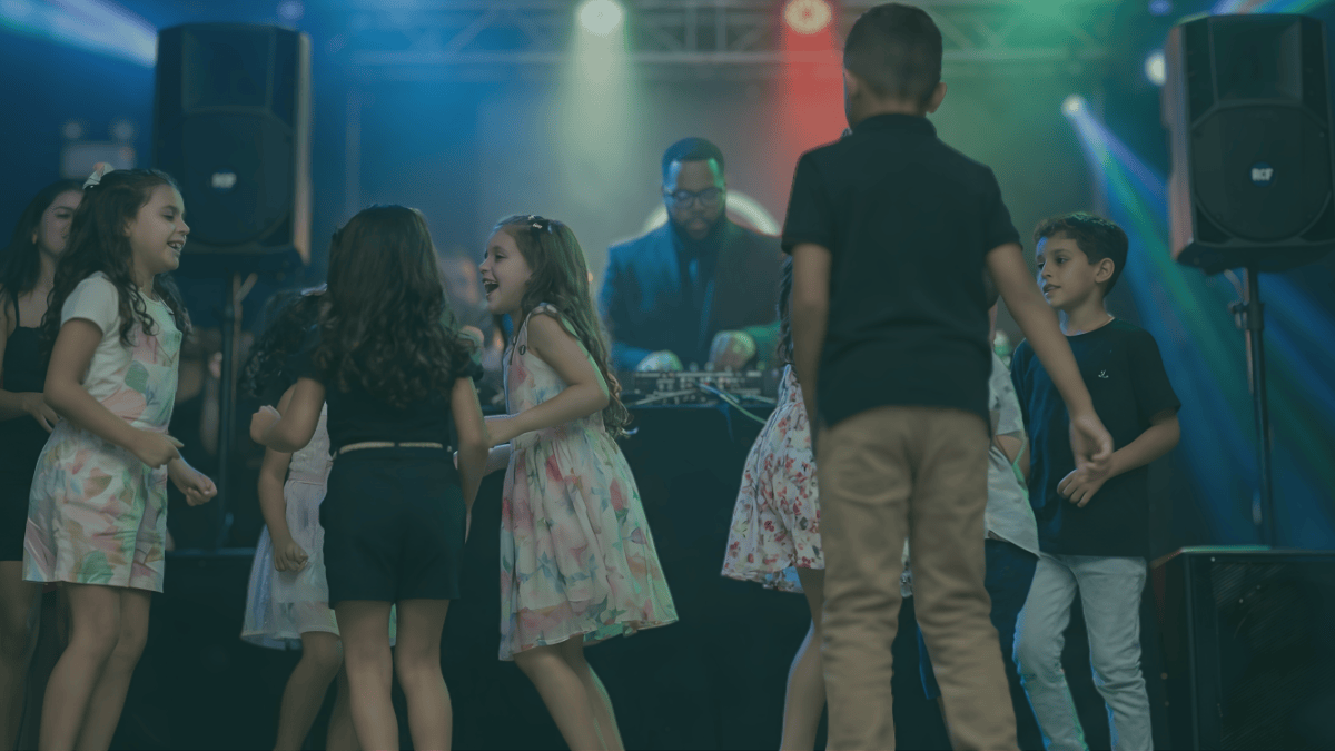 Group of children dancing and having fun near a DJ in a colorful party setting with stage lights.