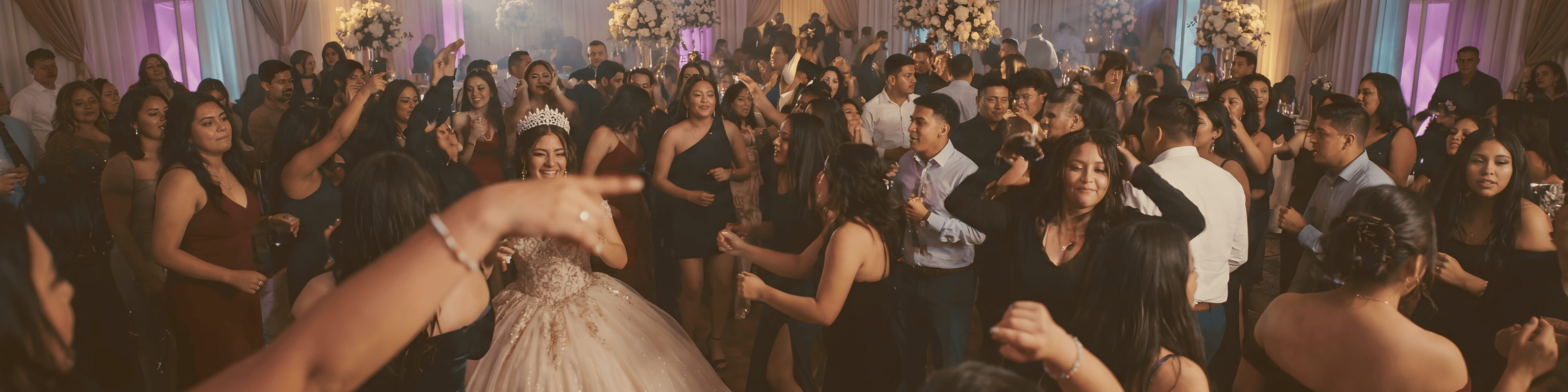 Large group of people dancing at a celebration with a woman in a white dress and tiara at the center.