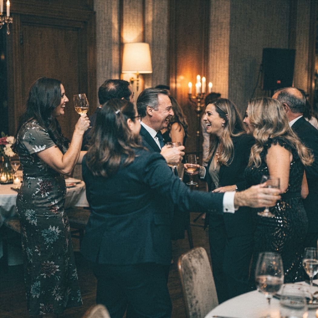 Group of people in formal attire laughing and toasting with drinks at an indoor social event.